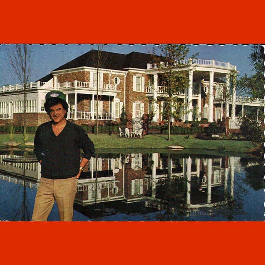 A photo of Conway Twitty's former home, with Conway posing in front of it. The property opened to the public as a tourist destination called "Twitty City" and was popular in the 1980s.